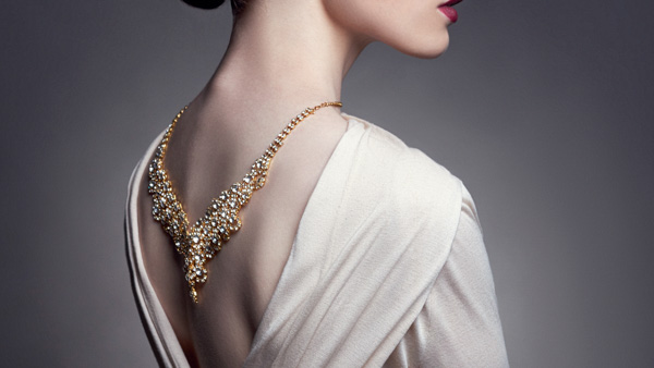 Image: Back view of a lady with a gold necklace drapped down her back.
