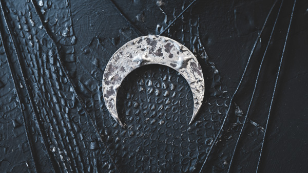 Image: A silver pendent in the shape of a crescent moon.